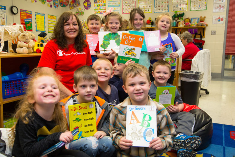 An elementary school teacher sits with her students as they hold up their favorite picture books in their Kentucky classroom. They are part of Save the Children's in school emergent reader program which provides training, tools and support schools need to accelerate reading growth for struggling readers.